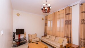 Una sala de estar con sofá, sillas, una mesa de centro, televisor y cortinas.