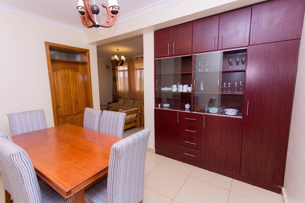A dining area with a wooden table and striped chairs, a red wooden cabinet with glass doors, and a wooden door.