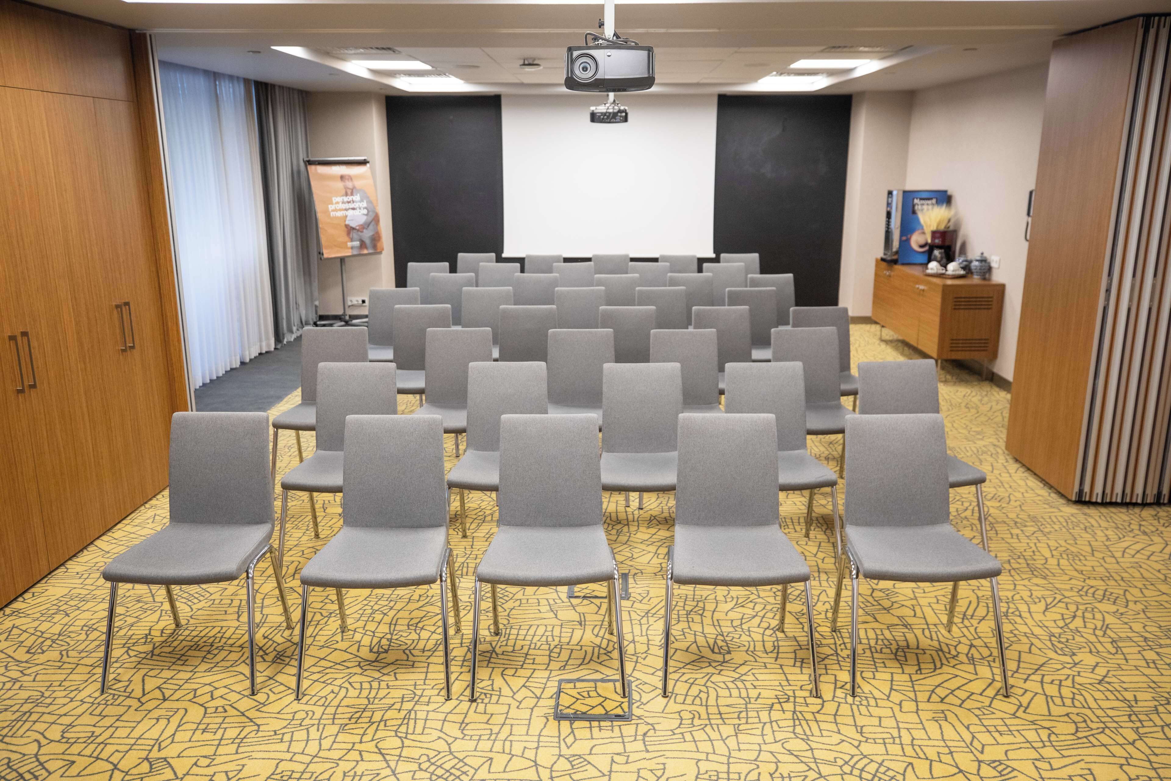 A conference room with rows of grey chairs, a projector screen, and a podium.