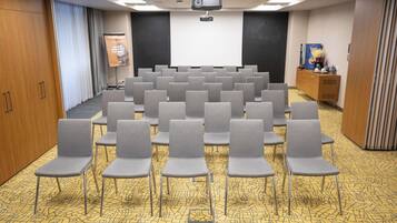 A conference room with rows of grey chairs, a projector screen, and a podium.