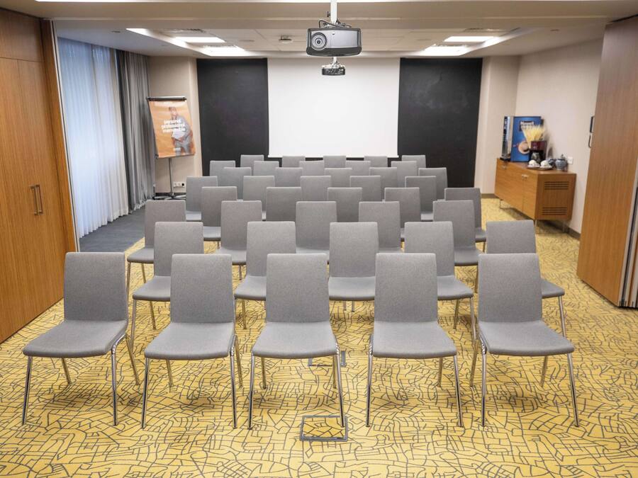 A conference room with rows of grey chairs, a projector screen, and a podium.