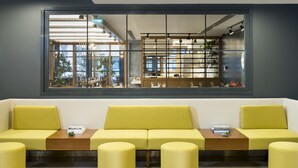 A modern interior with a yellow sofa set, a wooden coffee table, and a large window with a view of a bar area. - Park Inn by Radisson Istanbul Atasehir (Istanbul)