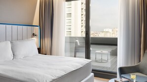 A modern hotel room with a large bed, a small round table, a chair, and a balcony with a city view. - Park Inn by Radisson Istanbul Atasehir (Istanbul)