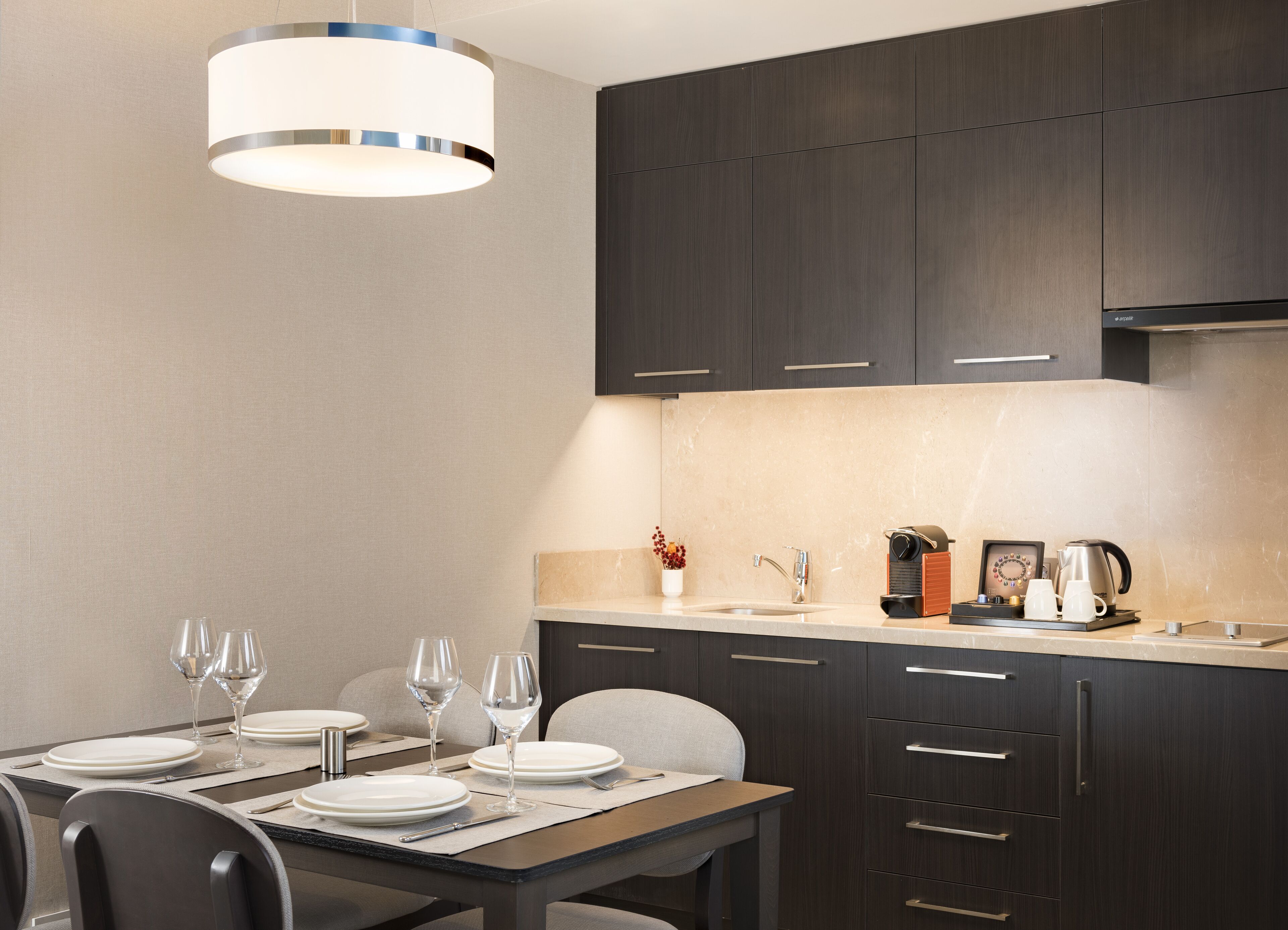 A modern kitchen with dark wood cabinets, a light countertop, and a hanging light fixture.