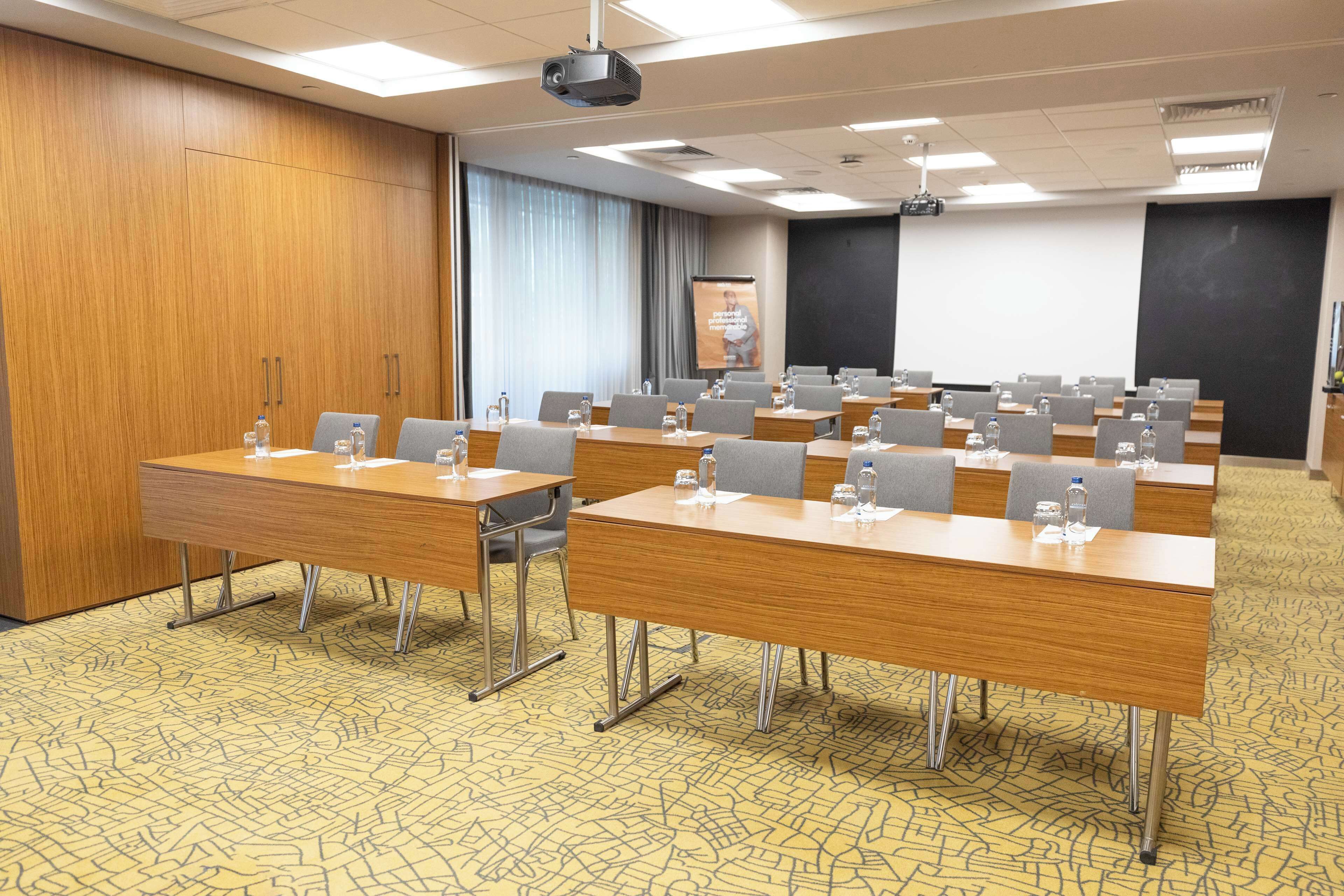 A conference room with multiple tables, chairs, and a projector screen.