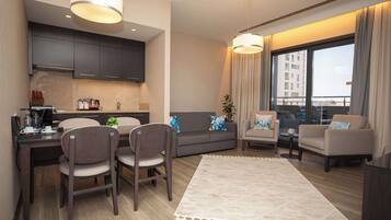 A modern living room with a dining area, grey sofas, a coffee table, and a large window with curtains.