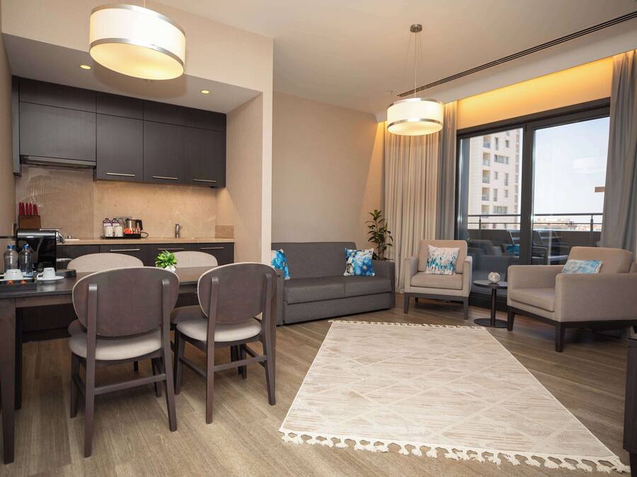 A modern living room with a dining area, grey sofas, a coffee table, and a large window with curtains.