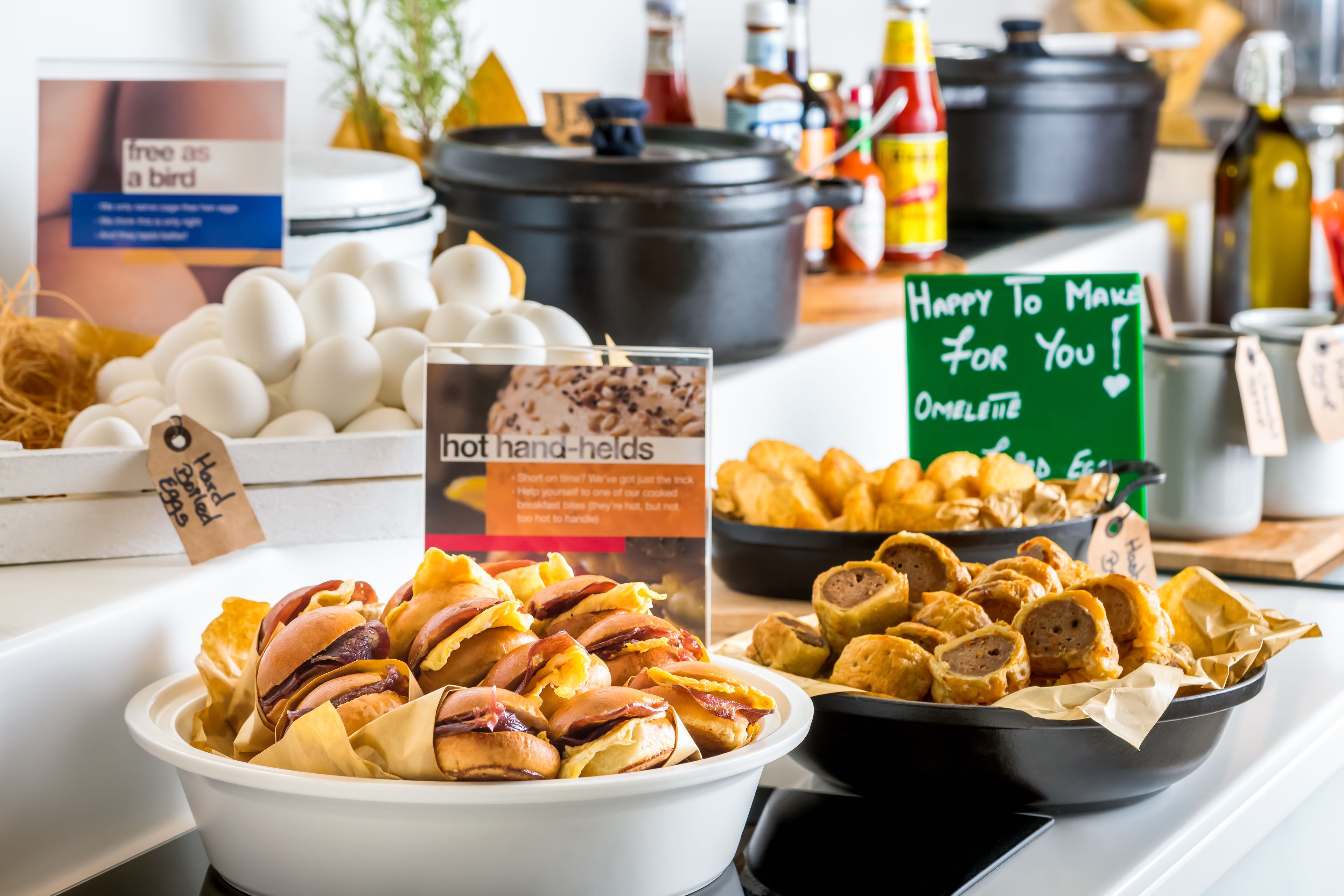 A buffet with various food items including hot hand-helds, eggs, and a sign offering omelette.