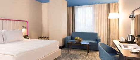 A hotel room with a bed, a sofa, a desk, and a chair.