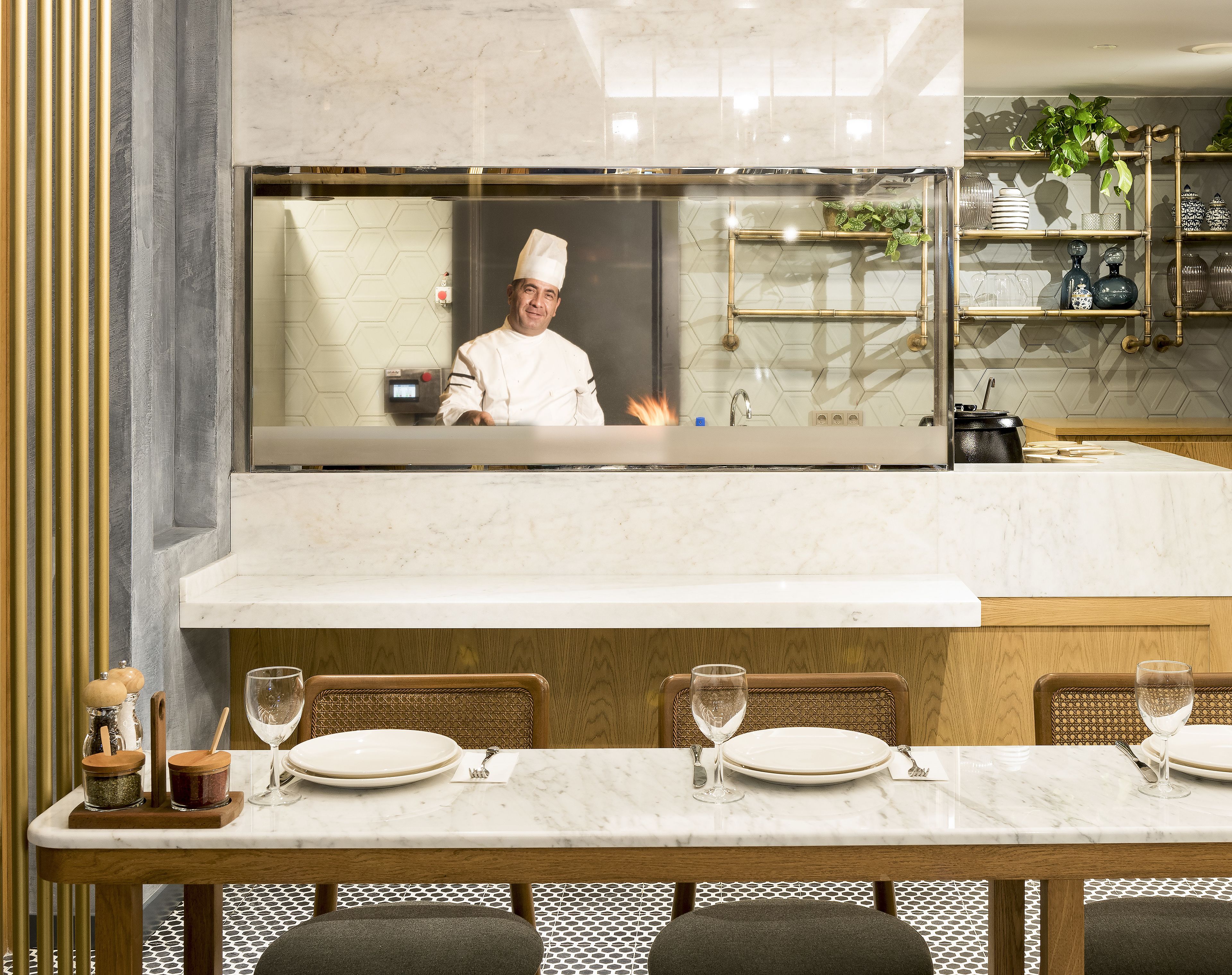 A modern kitchen with a marble countertop, a built-in stove, and a large screen displaying a chef.