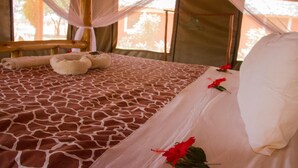 Una cama con una colcha de estampado de jirafa, un dosel y una única flor roja.