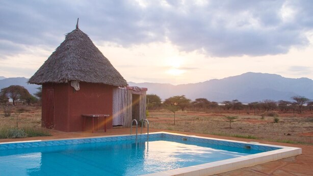 Una piscina con una cabaña de techo de paja y vistas a las montañas.