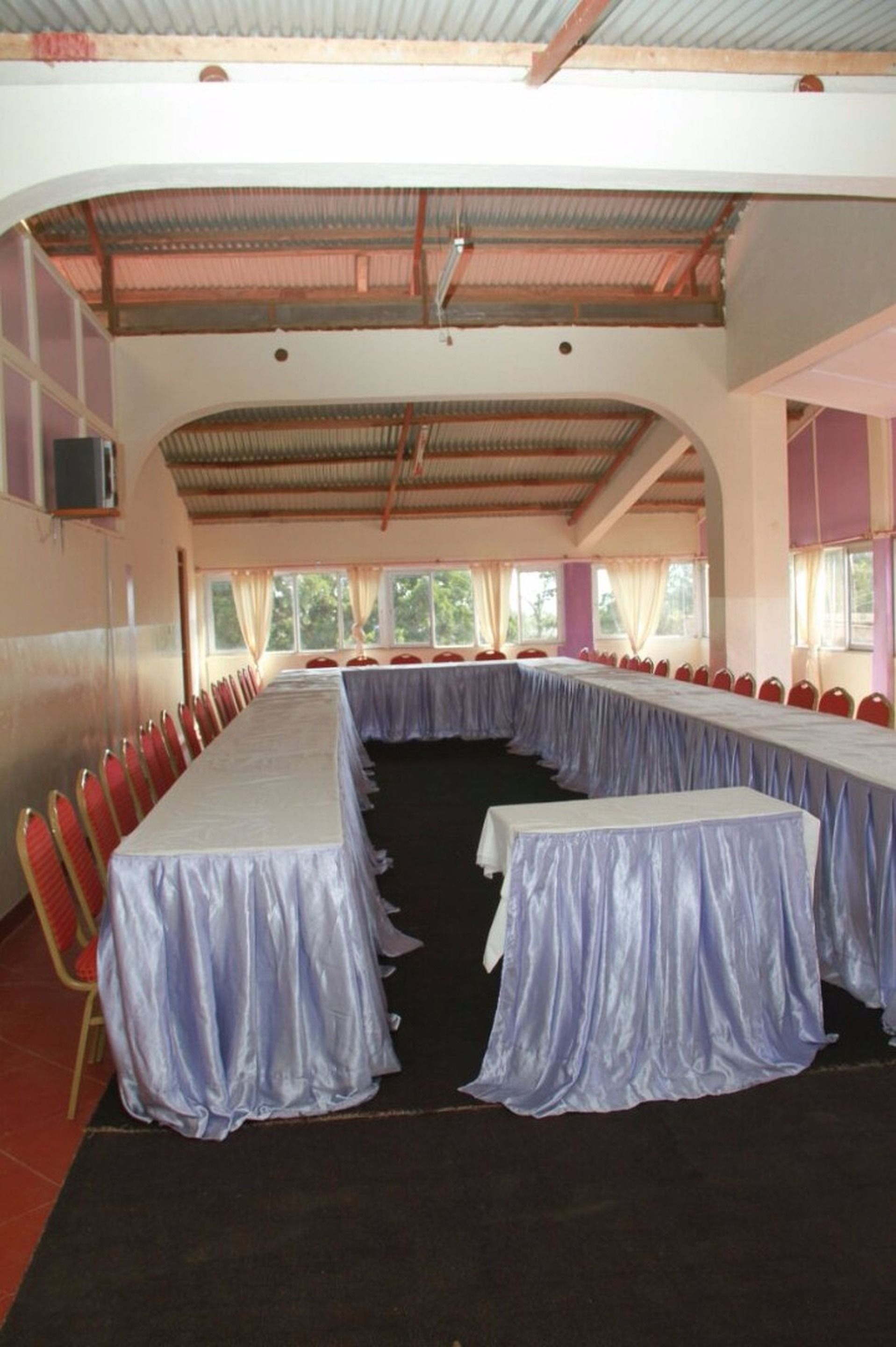 Un salón de conferencias con una mesa larga, sillas rojas y ventanas amplias.