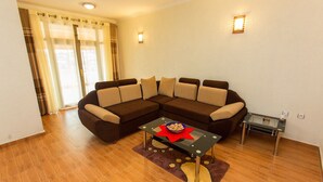 A living room with a brown sectional sofa, a glass coffee table with a bowl, and a small side table. - Eden Escape Apartments (Kigali)