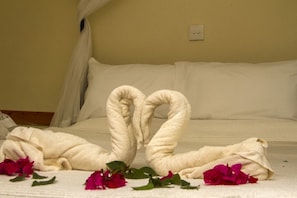 A bed with white linens and two towels arranged in a heart shape on the bed.
