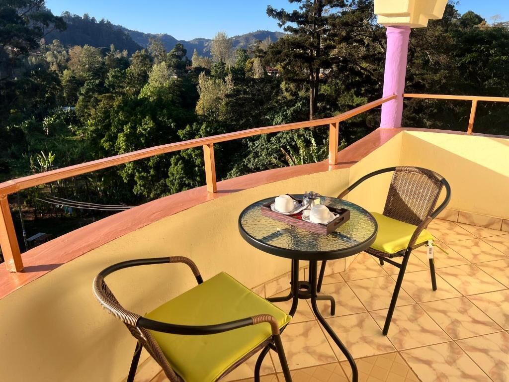 A balcony with two chairs and a table, overlooking a mountainous landscape.