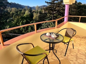 A balcony with two chairs and a table, overlooking a mountainous landscape.