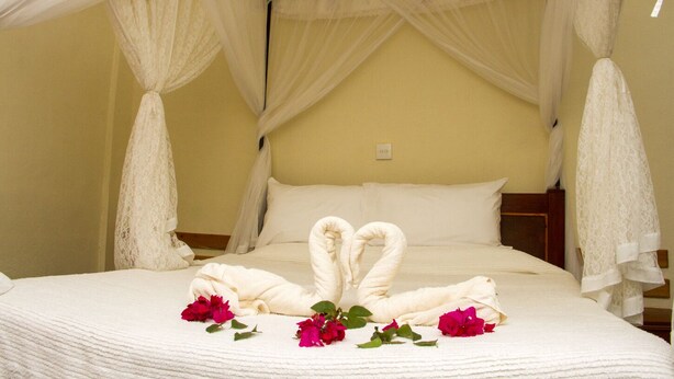 A bed with a canopy, white pillows, and a towel arrangement in the shape of a heart.