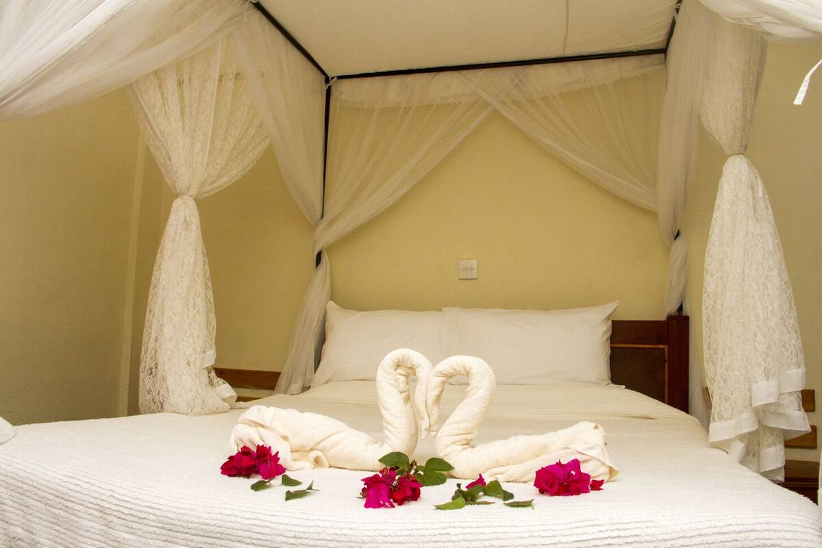 Una cama con dosel, almohadas blancas y una disposición de toallas en forma de corazón.