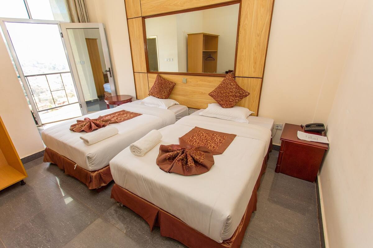 A hotel room with two beds, a large mirror, a wooden wardrobe, and a small desk with a telephone.