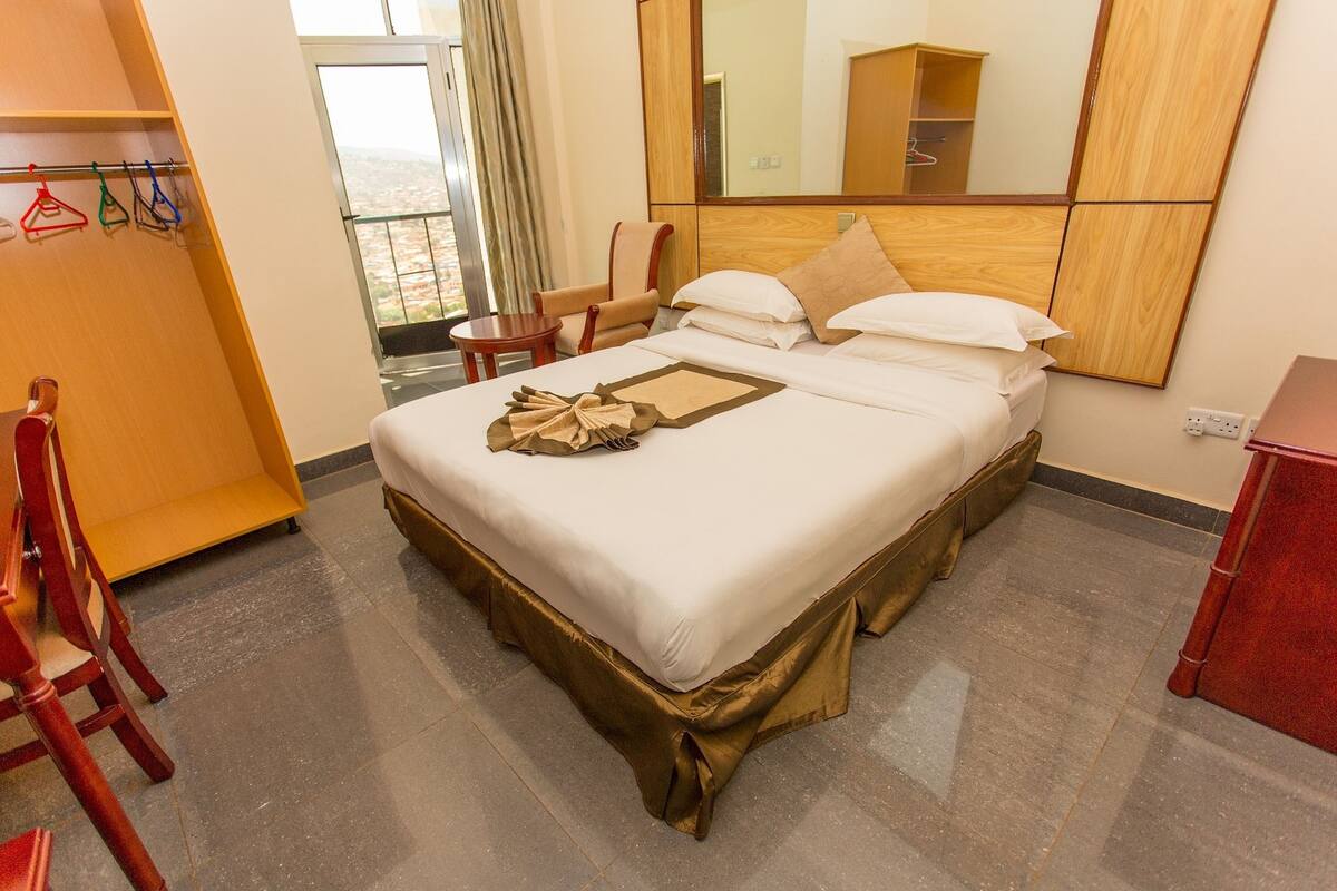 A hotel room with a bed, a chair, a table, a mirror, and a wardrobe.