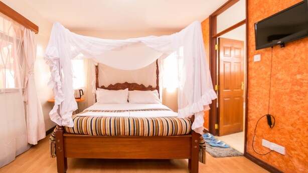 Una cama de madera con dosel, un televisor montado en la pared y una puerta de madera al fondo.