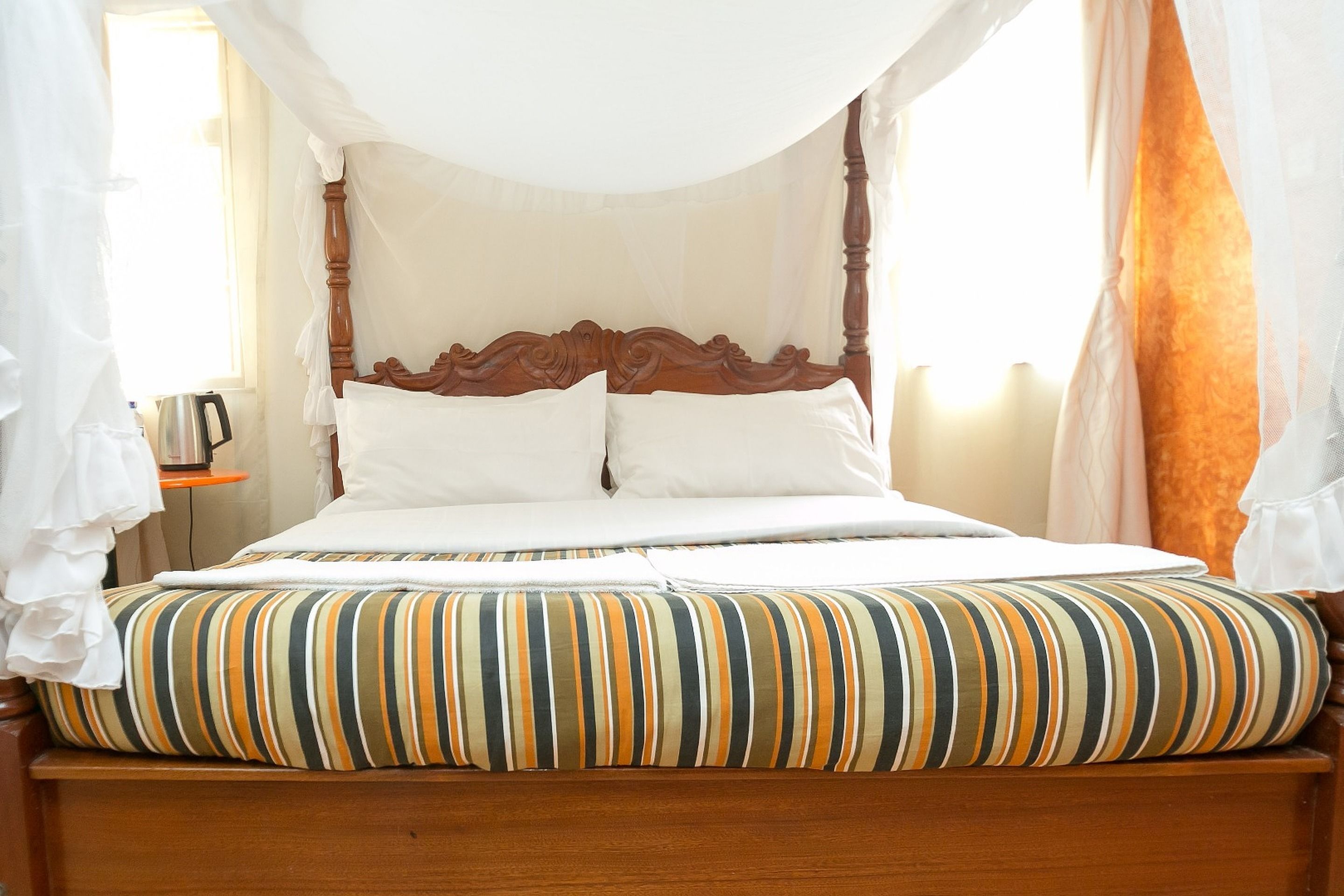 A four-poster canopy bed with white linens and striped pillows.