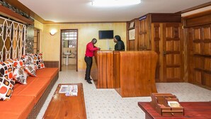 Un área de recepción con un mostrador de madera, un sofá con cojines estampados, un banco de madera y un suelo de baldosas.