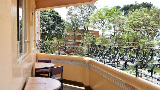 A balcony with two tables and chairs, a metal railing, and a view of trees and buildings. - Maru B Courts Hotel (Nyeri)