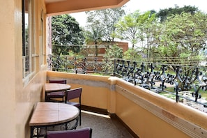A balcony with two tables and chairs, a metal railing, and a view of trees and buildings. - Maru B Courts Hotel (Nyeri)