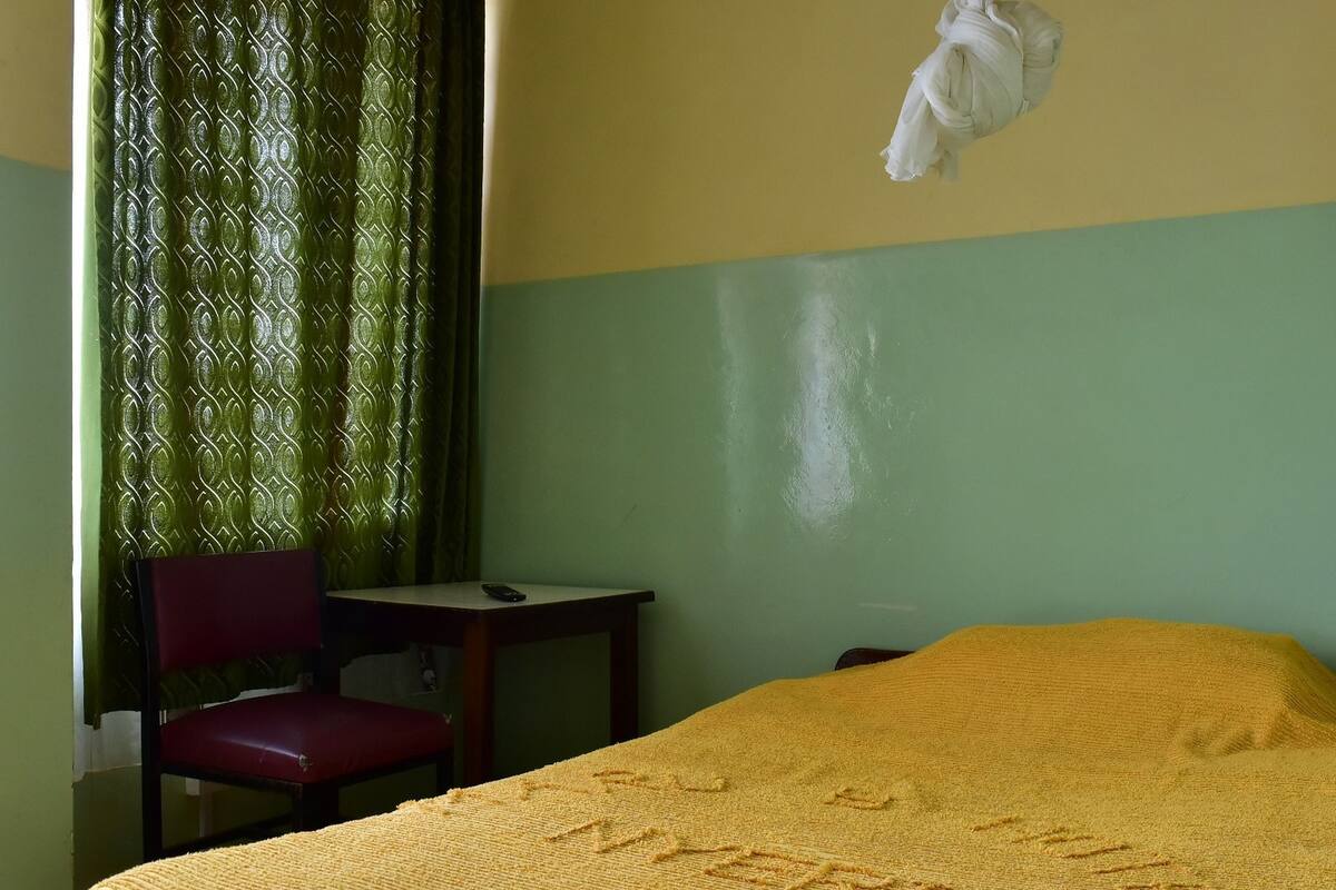 Ein Zimmer mit einem Bett, einem Sessel, einem Tisch und einem Vorhang.