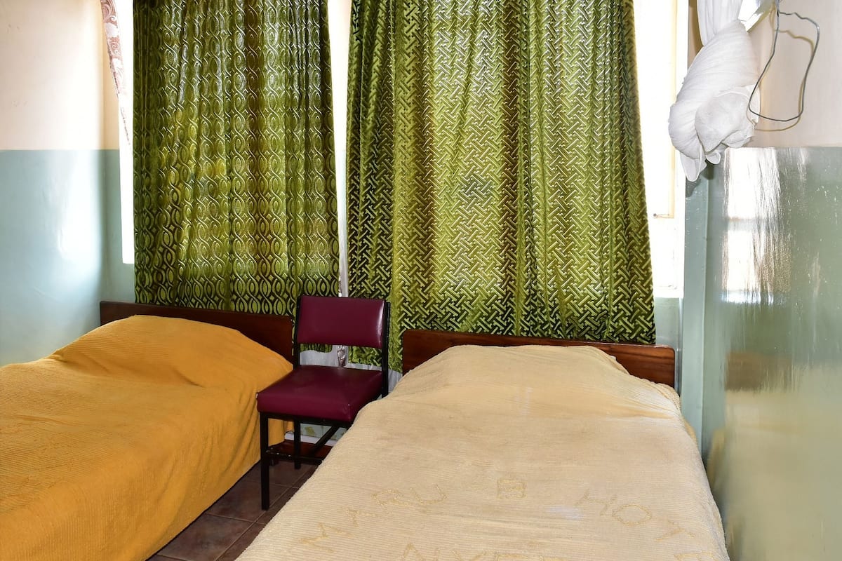 Ein Zimmer mit zwei Betten, einem Sessel und gemusterten Vorhängen.