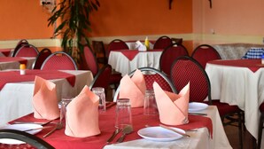 A restaurant with tables set with white tablecloths, red chairs, and pink napkins. - Maru B Courts Hotel (Nyeri)