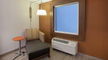 Una habitación pequeña con una cama individual, una lámpara de pie, una ventana y un aire acondicionado instalado en la pared.