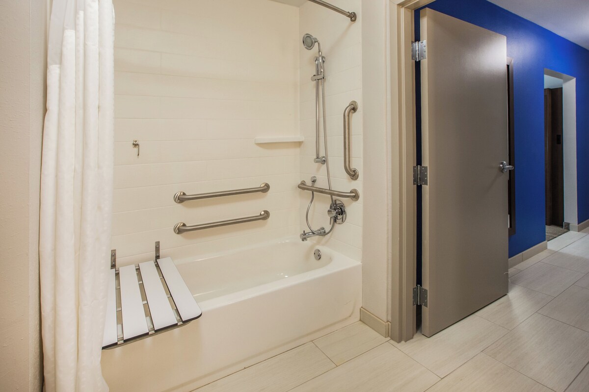 Une salle de bain moderne équipée d’une baignoire, de barres d’appui et d’un pommeau de douche.
