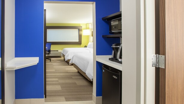 A hotel room with a bed, a desk with a coffee maker, and a TV on the wall. - Holiday Inn Express & Suites Atlanta N - Woodstock by IHG (Woodstock)