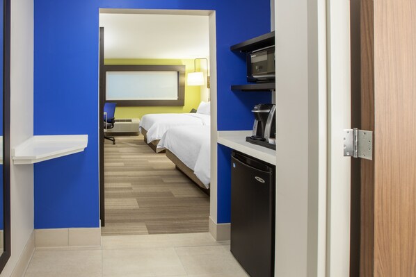 Une chambre d’hôtel avec un lit, un bureau doté d’une machine à café et un téléviseur fixé au mur.
