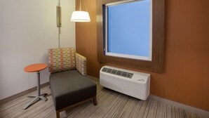A compact hotel room with a small bed, a single table, a window with a view, and a wall-mounted air conditioner. - Holiday Inn Express & Suites Atlanta N - Woodstock by IHG (Woodstock)