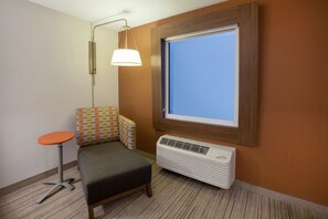 Une chambre d’hôtel de taille réduite, avec un petit lit, une table, une fenêtre donnant sur un paysage agréable et un climatiseur fixé au mur.