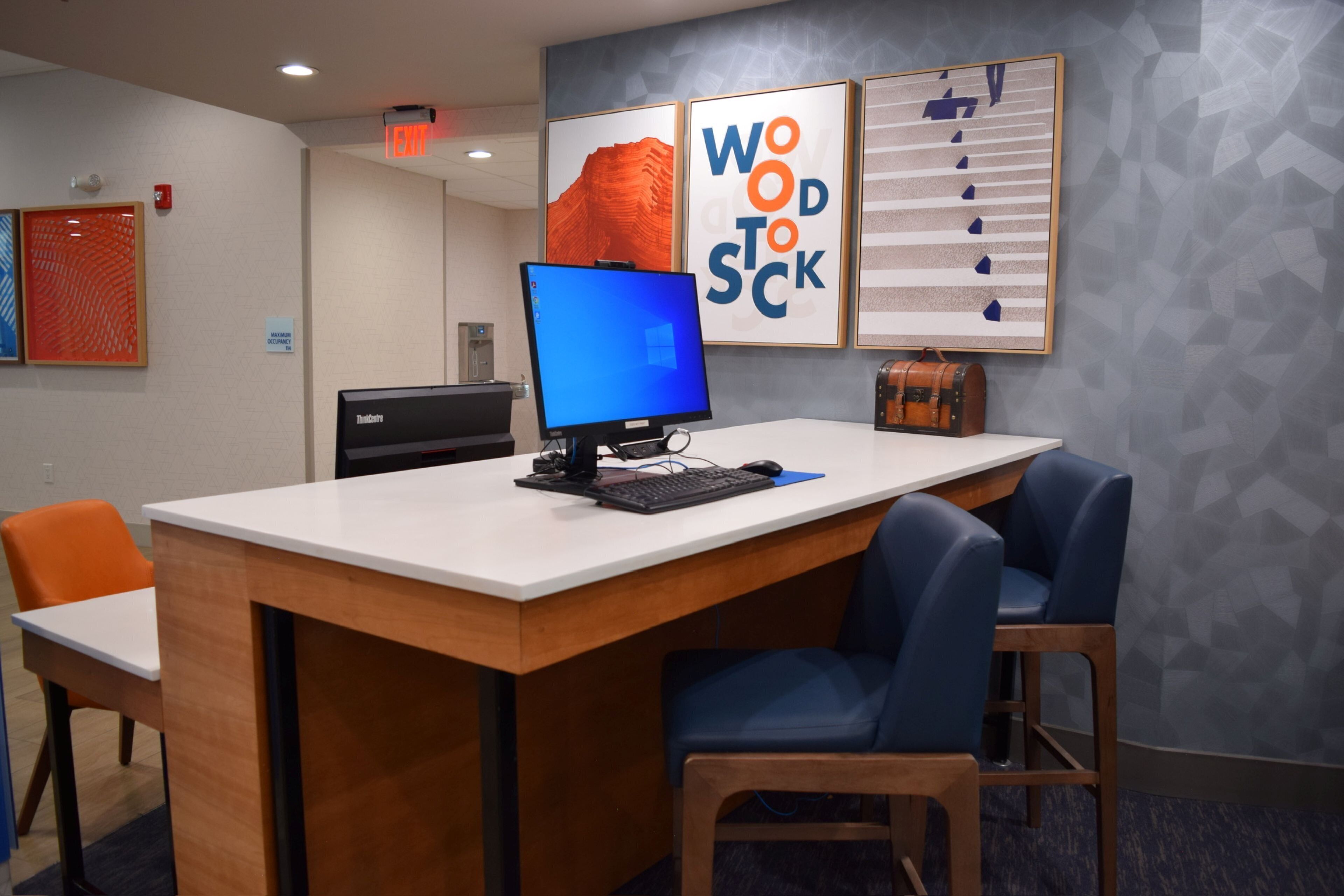 A reception desk with a computer, a sign indicating maximum occupancy, and framed artwork on the wall.