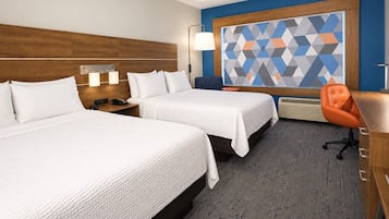 A hotel room with two beds, a desk, a chair, a large geometric wall art, and a lamp.