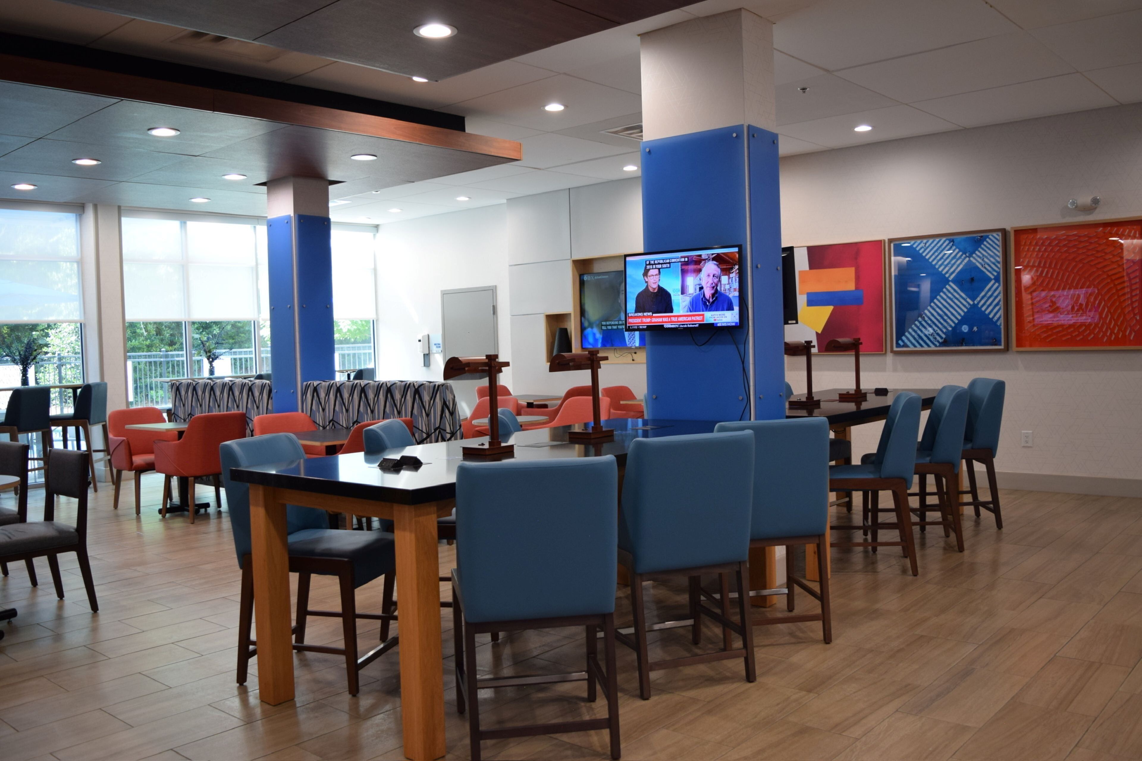 Un restaurante con varias mesas y sillas, una pantalla de televisión y obras de arte en las paredes.