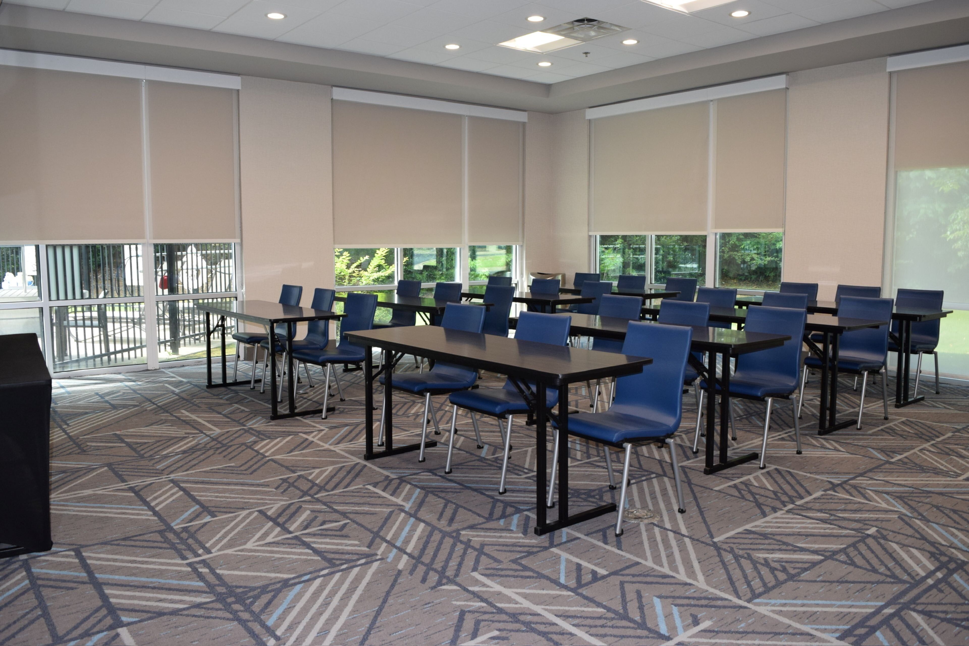 A conference room with multiple tables and chairs, large windows, and a patterned carpet.