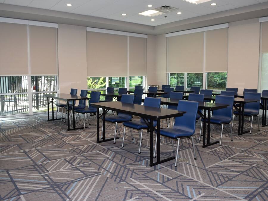 A conference room with multiple tables and chairs, large windows, and a patterned carpet.