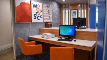 A modern office space with a desk, two orange chairs, a computer, and framed artwork on the wall.