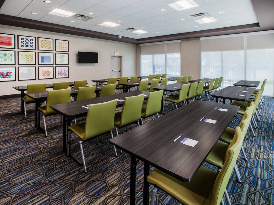 A conference room with multiple tables and chairs, a flat-screen TV mounted on the wall, and framed artwork on the wall.