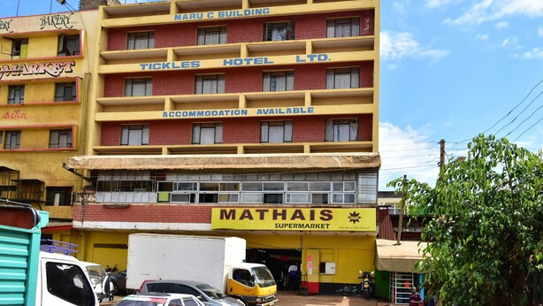 A multi-story building with a yellow and red facade, housing a supermarket named Mathais, a hotel named Tickles Hotel Ltd., and a market. - Tickles Hotel (Nyeri)