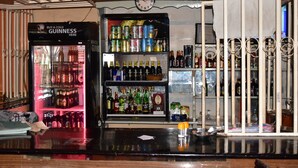 A bar area with a Guinness refrigerator, shelves of various alcoholic beverages, and a counter with a glass and a spoon. - Tickles Hotel (Nyeri)