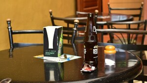 A table with a bottle of St. Louis beer, a salt shaker, and a menu on a glass table in a restaurant setting. - Tickles Hotel (Nyeri)