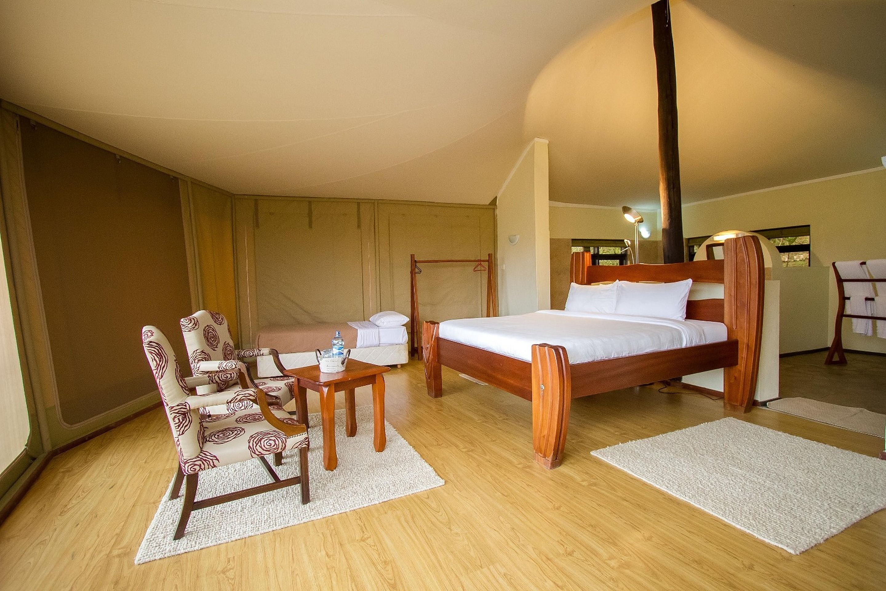 A bedroom with a wooden bed, a wooden chair, a small table with a teapot, and a white sofa.